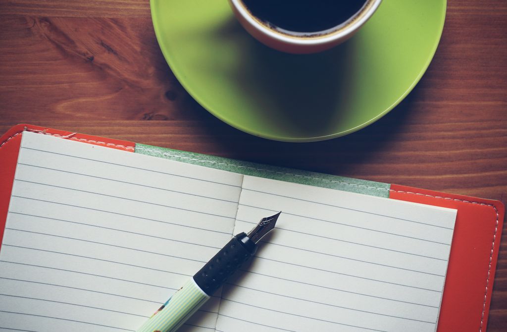 A relaxing setting featuring a cup of coffee, a fountain pen, and an open notebook on a wooden table.